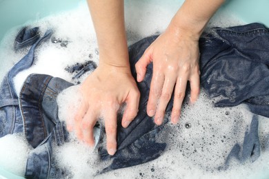 Woman washing denim clothes with soap and water in basin, closeup