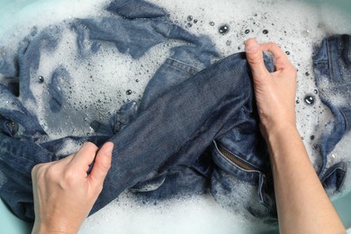 Woman washing denim clothes with soap and water in basin, top view