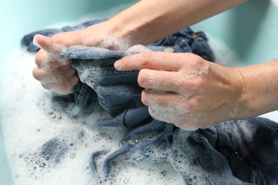 Woman washing denim clothes with soap and water in basin, closeup