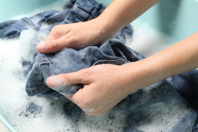 Photo of Woman washing denim clothes with soap and water in basin, closeup