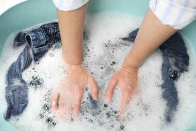 Woman washing denim clothes with soap and water in basin, top view