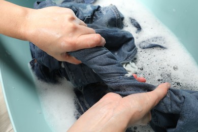 Woman washing denim clothes with soap and water in basin, closeup