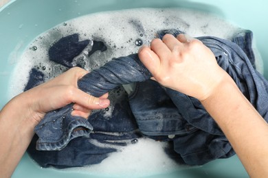 Woman washing denim clothes with soap and water in basin, top view