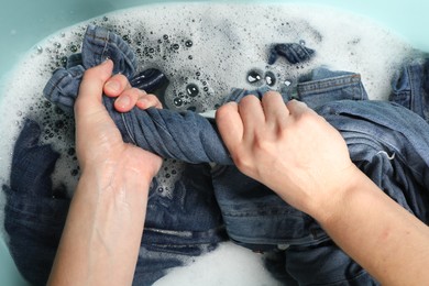 Woman washing denim clothes with soap and water in basin, top view