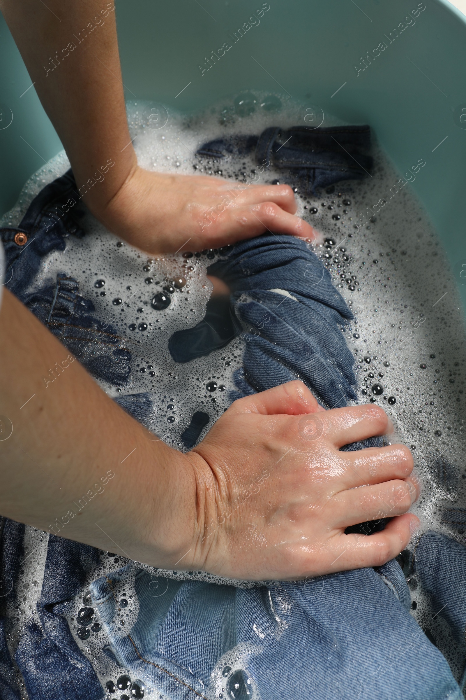 Photo of Woman washing denim clothes in basin, closeup