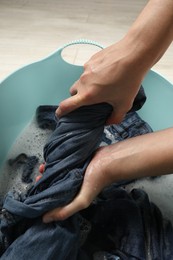 Woman washing denim clothes with soap and water in basin, closeup