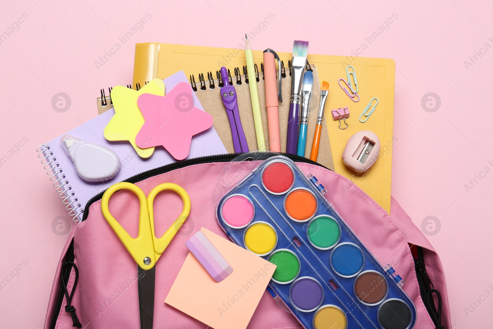 Photo of Backpack and different school stationery on pink background, top view