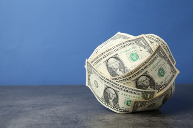 Photo of Ball made of dollar banknotes on grey textured table against blue background, space for text