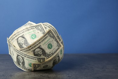 Photo of Ball made of dollar banknotes on grey textured table against blue background, space for text