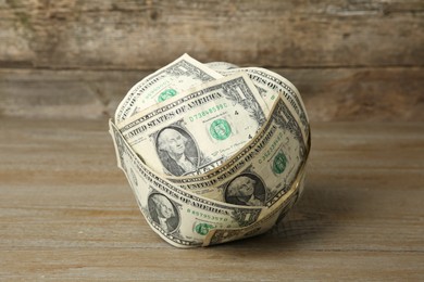 Photo of Ball made of dollar banknotes on wooden table, closeup