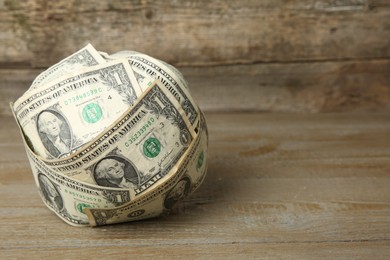 Photo of Ball made of dollar banknotes on wooden table, closeup. Space for text