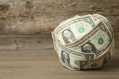 Photo of Ball made of dollar banknotes on wooden table, closeup. Space for text