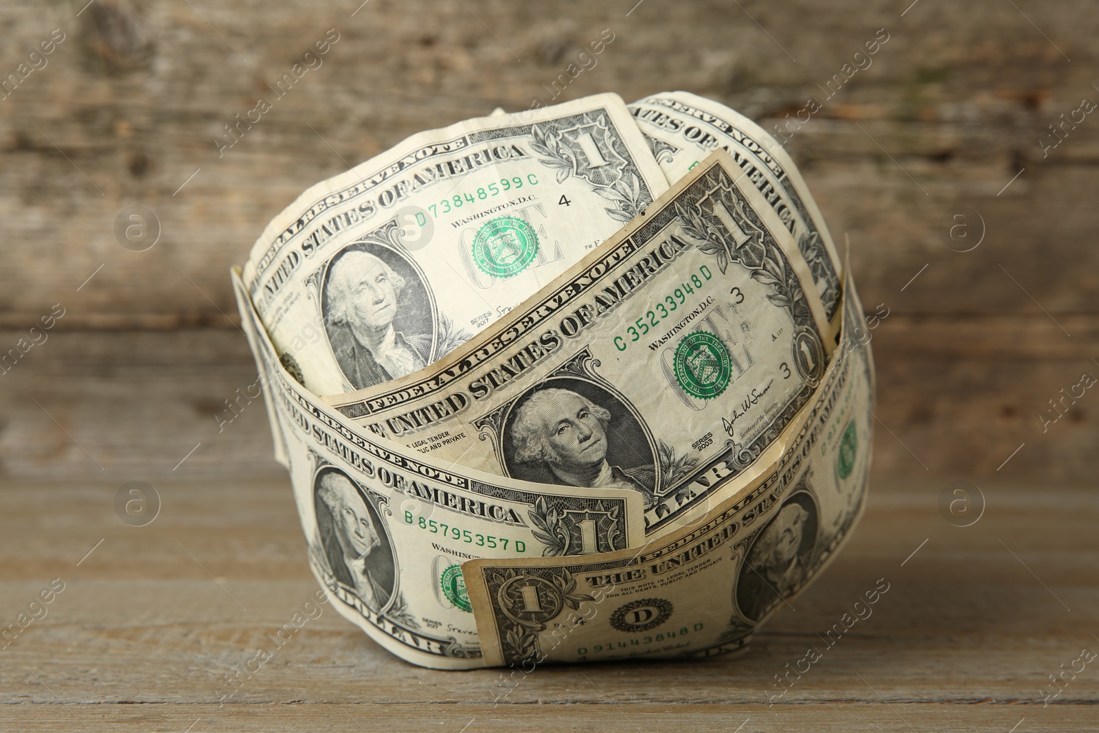 Photo of Ball made of dollar banknotes on wooden table, closeup