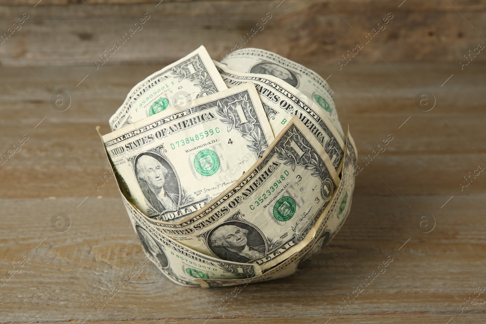 Photo of Ball made of dollar banknotes on wooden table