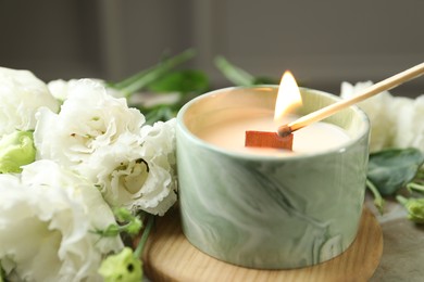 Photo of Lighting candle at table with beautiful flowers, closeup