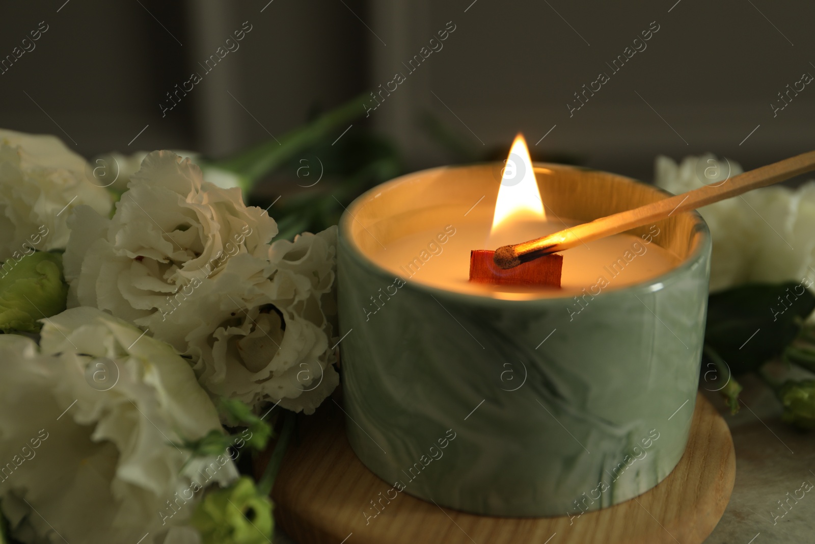 Photo of Lighting candle at table with beautiful flowers, closeup