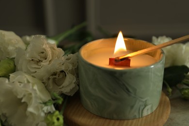 Lighting candle at table with beautiful flowers, closeup