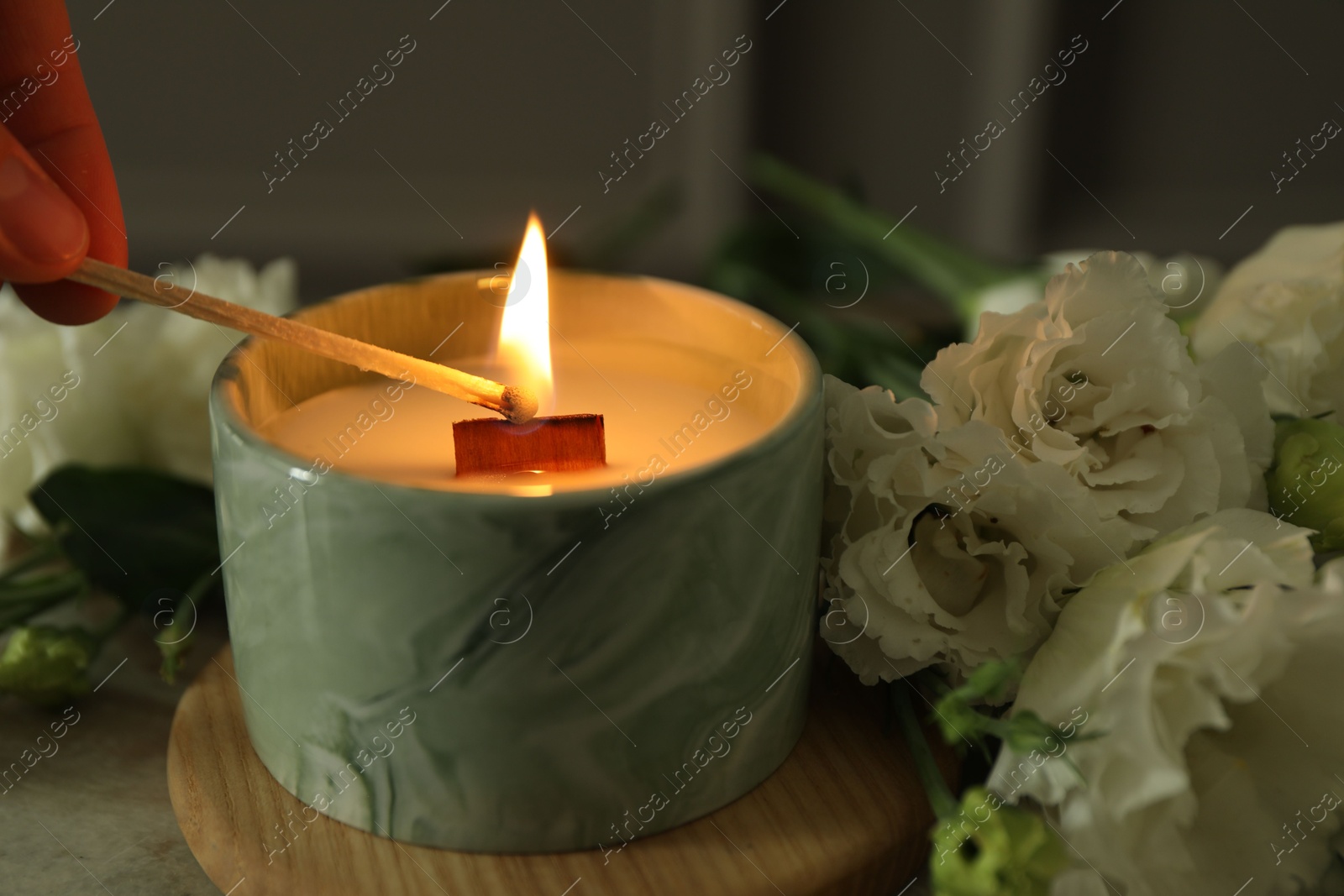 Photo of Woman lighting candle at table with beautiful flowers, closeup