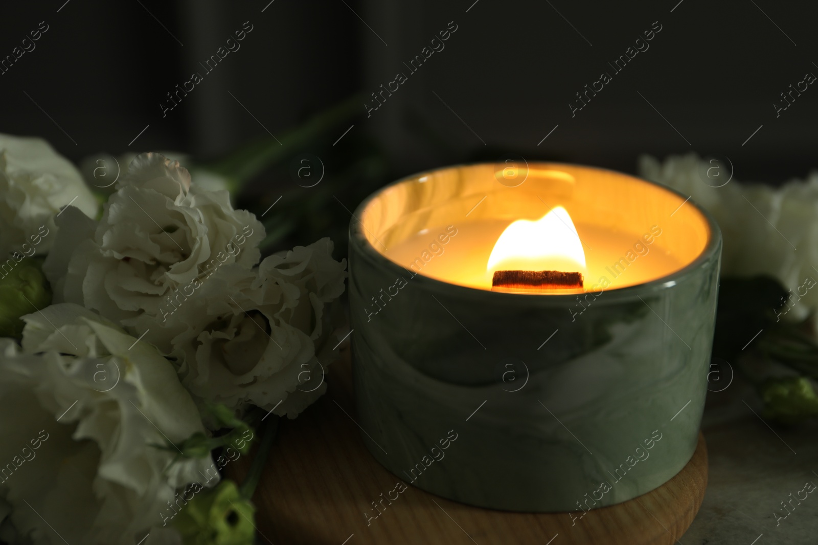 Photo of Burning candle and beautiful flowers on table, closeup