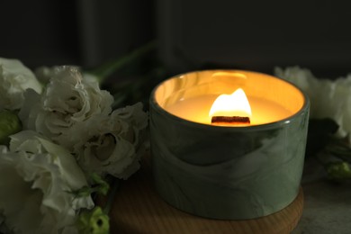 Photo of Burning candle and beautiful flowers on table, closeup