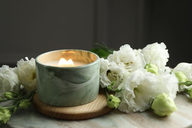 Burning candle and beautiful flowers on marble table, closeup