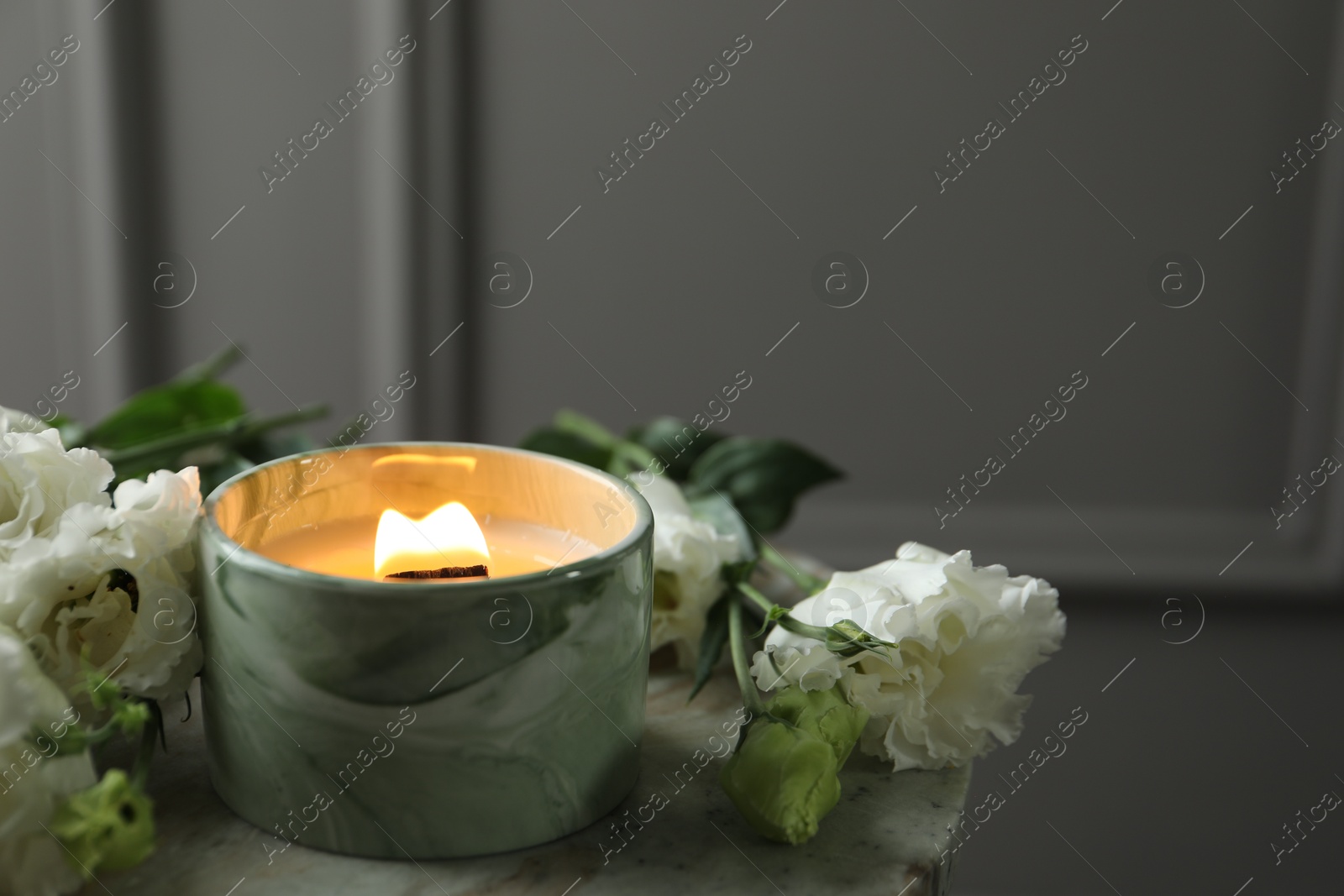 Photo of Burning candle and beautiful flowers on marble table. Space for text