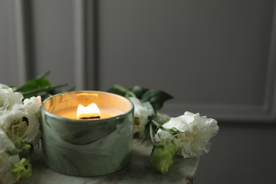 Burning candle and beautiful flowers on marble table. Space for text