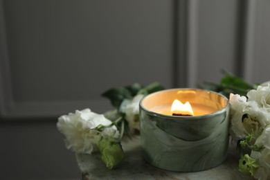 Burning candle and beautiful flowers on marble table. Space for text