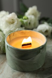 Burning candle and beautiful flowers on marble table, closeup