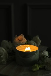 Burning candle and beautiful flowers on marble table, closeup. Space for text