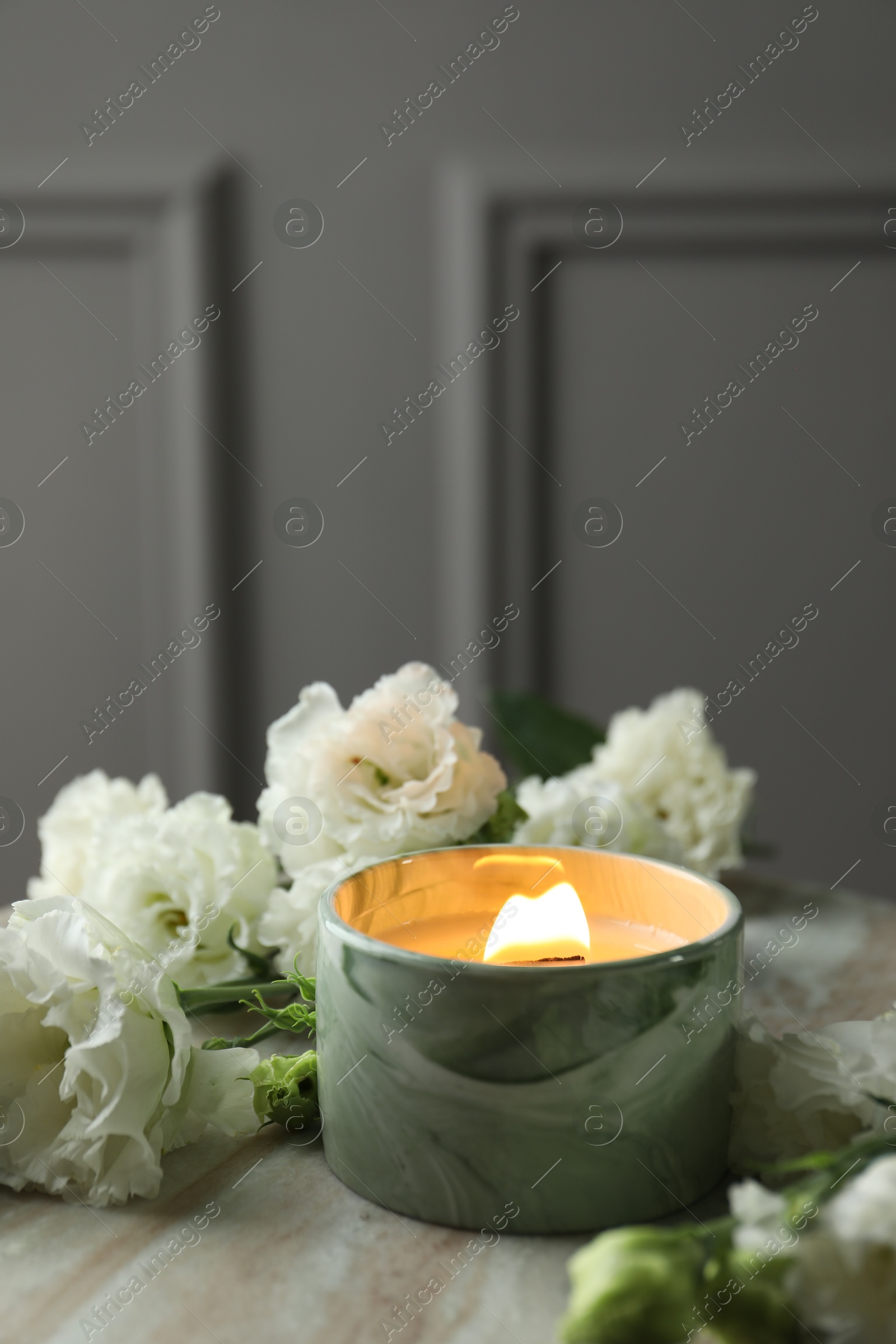 Photo of Burning candle and beautiful flowers on marble table, closeup. Space for text