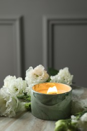 Burning candle and beautiful flowers on marble table, closeup. Space for text