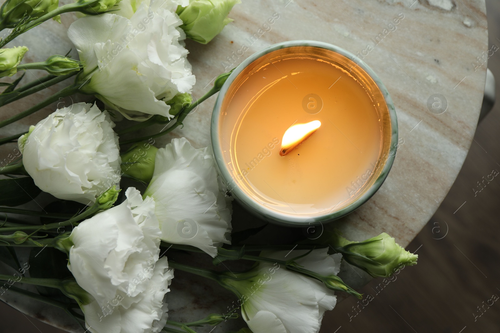 Photo of Burning candle and beautiful flowers on marble table, top view