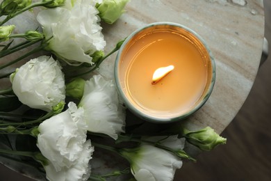 Photo of Burning candle and beautiful flowers on marble table, top view