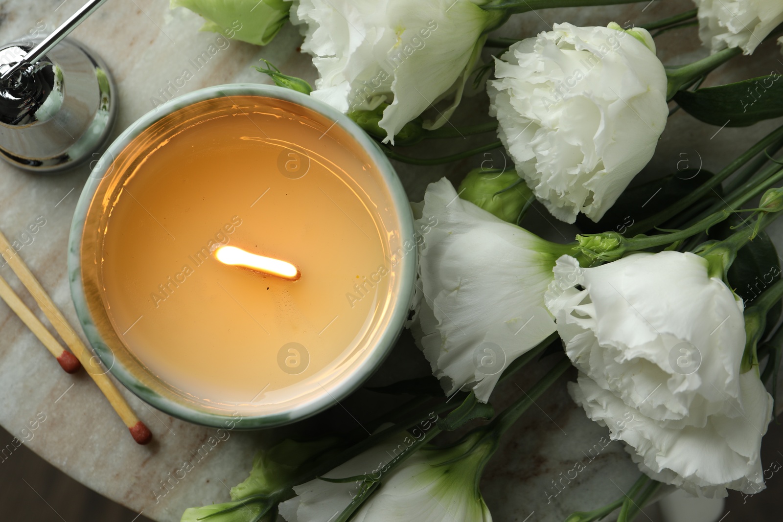 Photo of Burning candle and beautiful flowers on marble table, top view