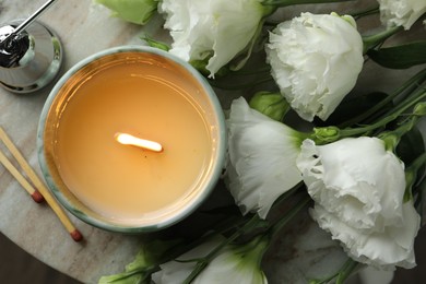 Burning candle and beautiful flowers on marble table, top view