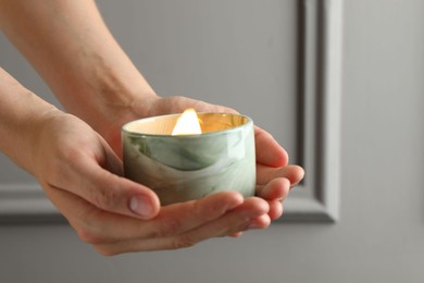 Woman holding burning candle against grey wall, closeup