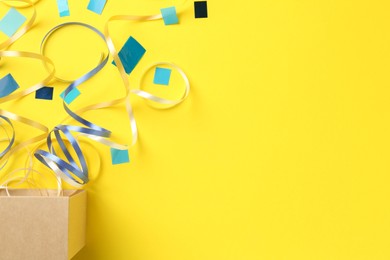 Photo of Box with confetti and party streamers on yellow background, flat lay. Space for text