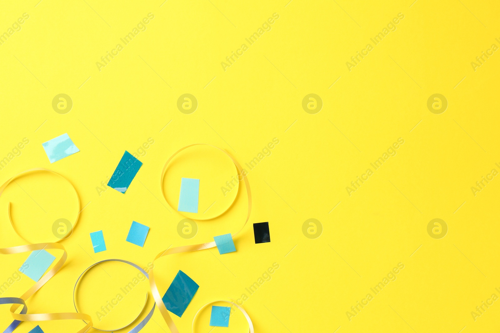 Photo of Beautiful confetti and party streamers on yellow background, flat lay. Space for text