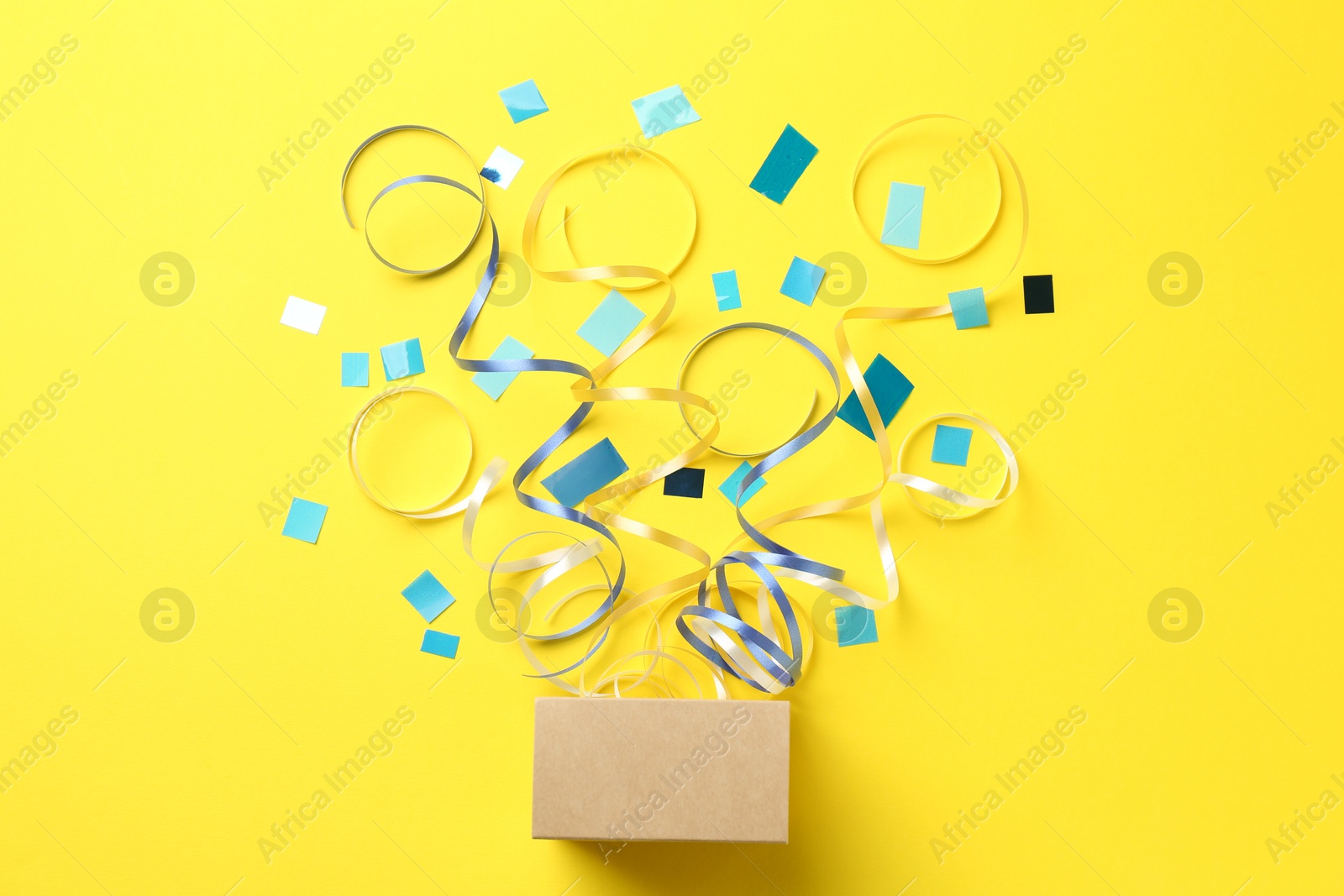 Photo of Box with confetti and party streamers on yellow background, flat lay