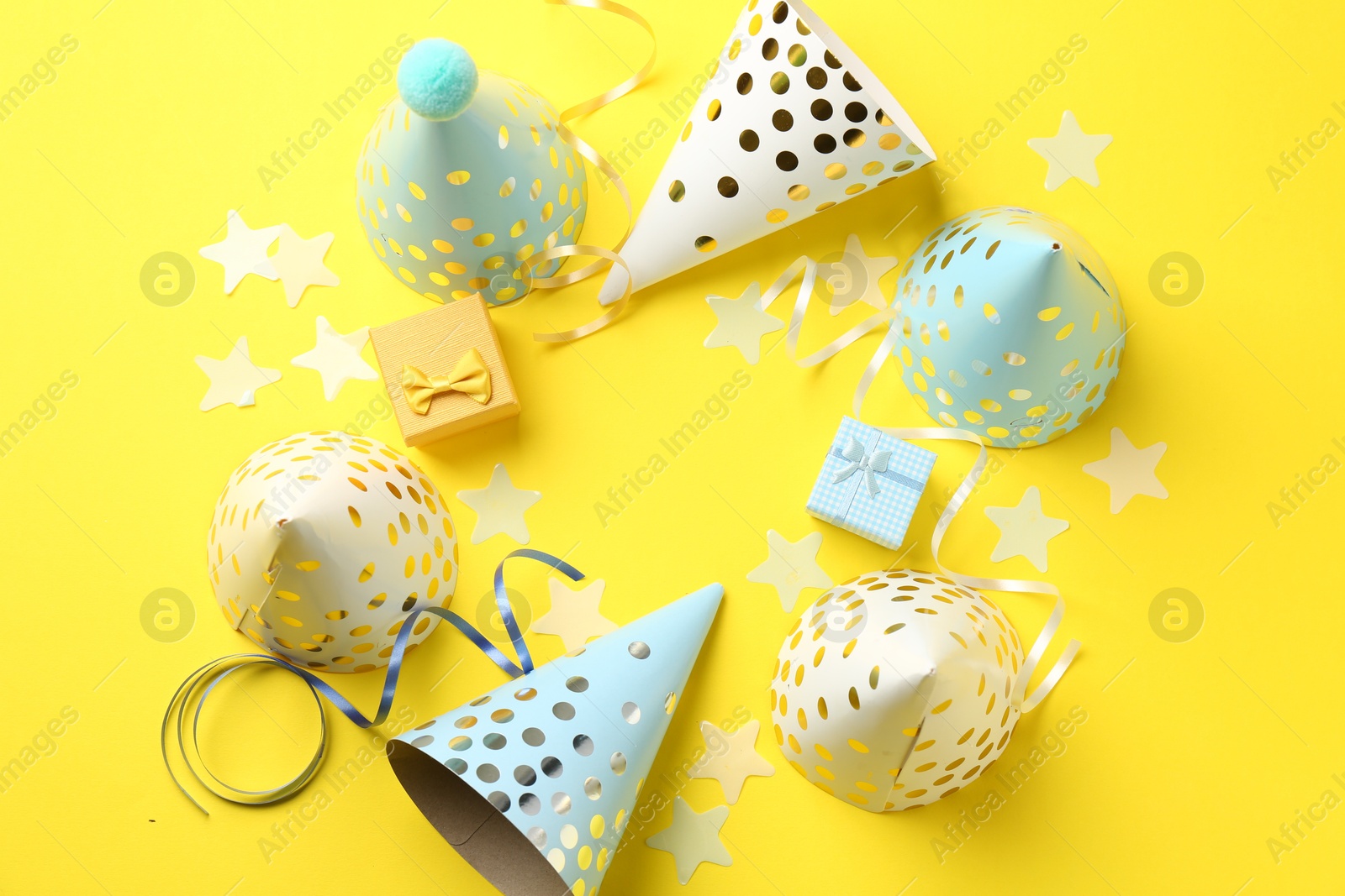 Photo of Party hats, gift boxes, confetti and streamers on yellow background, flat lay