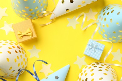 Frame of party hats, gift boxes, confetti and streamers on yellow background, flat lay. Space for text