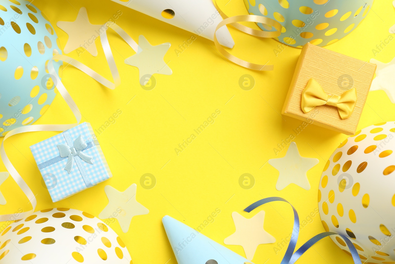 Photo of Frame of party hats, gift boxes, confetti and streamers on yellow background, flat lay. Space for text