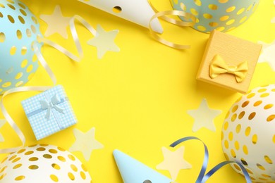 Frame of party hats, gift boxes, confetti and streamers on yellow background, flat lay. Space for text