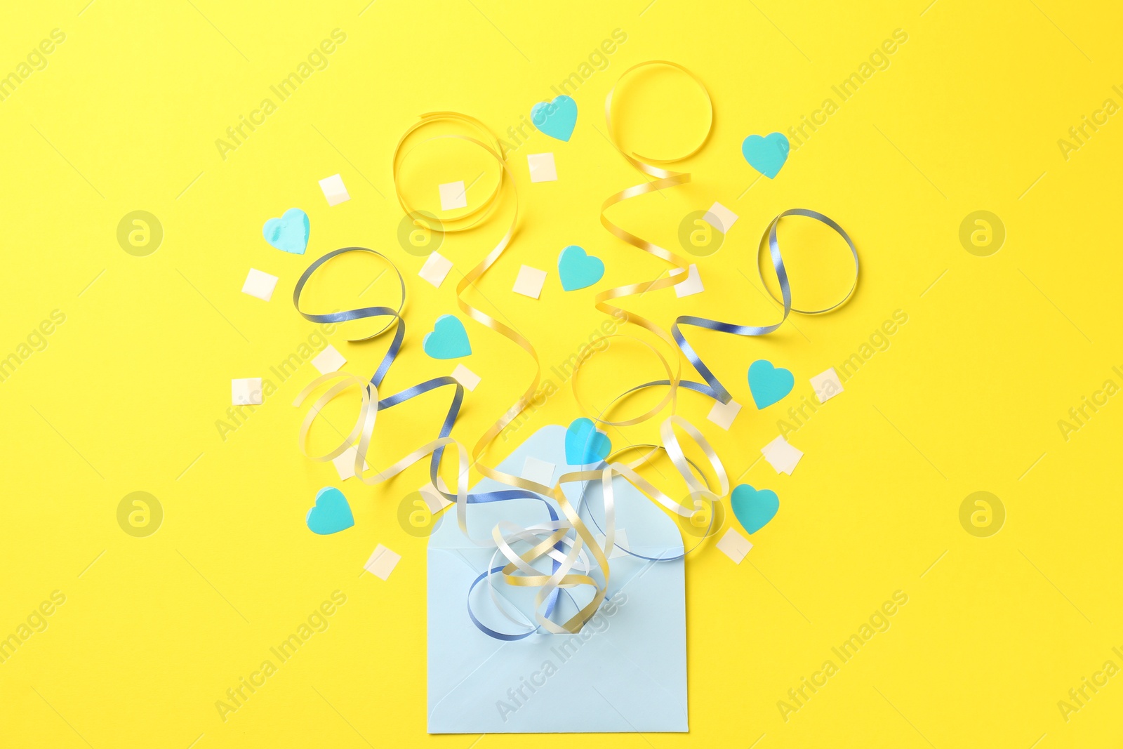 Photo of Envelope with confetti and party streamers on yellow background, flat lay