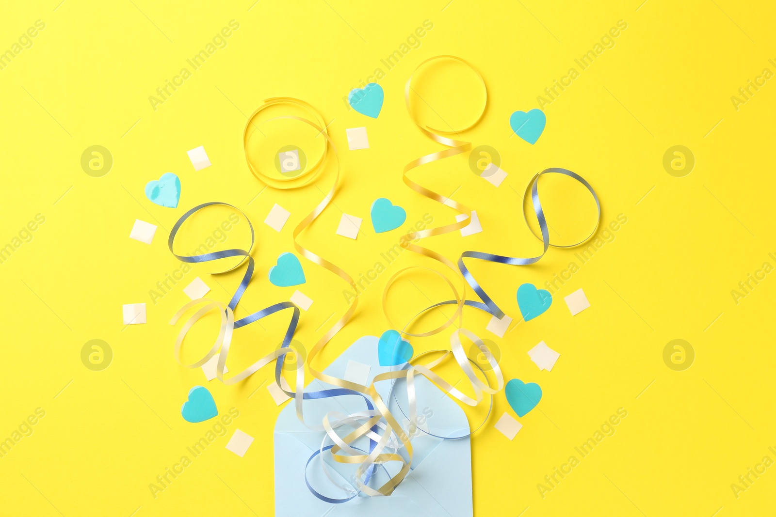 Photo of Envelope with confetti and party streamers on yellow background, flat lay