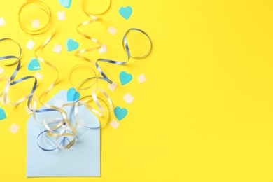 Photo of Envelope with confetti and party streamers on yellow background, flat lay. Space for text