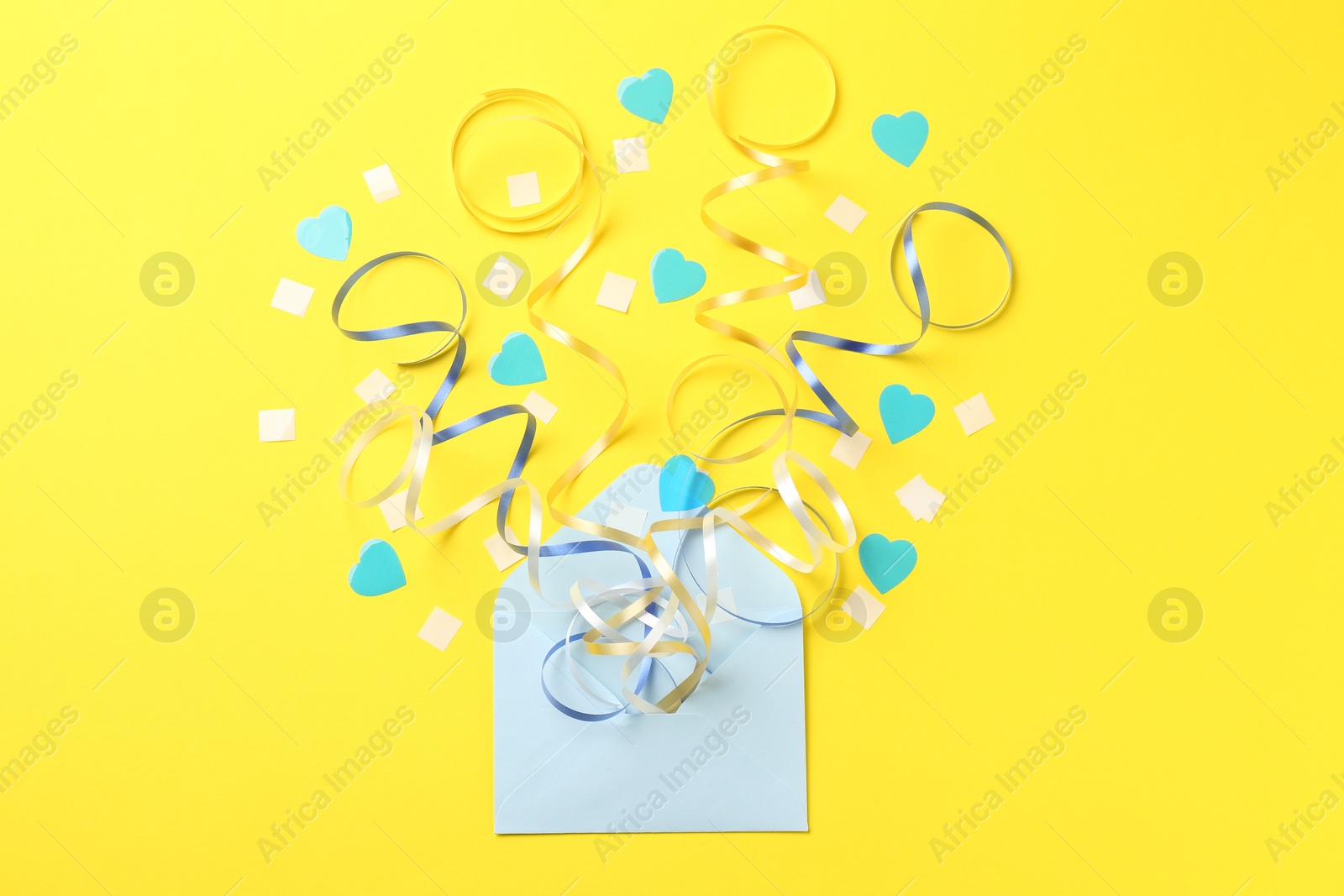 Photo of Envelope with confetti and party streamers on yellow background, flat lay