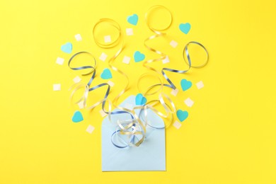 Photo of Envelope with confetti and party streamers on yellow background, flat lay