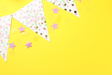 Confetti and garland on yellow background, flat lay. Space for text